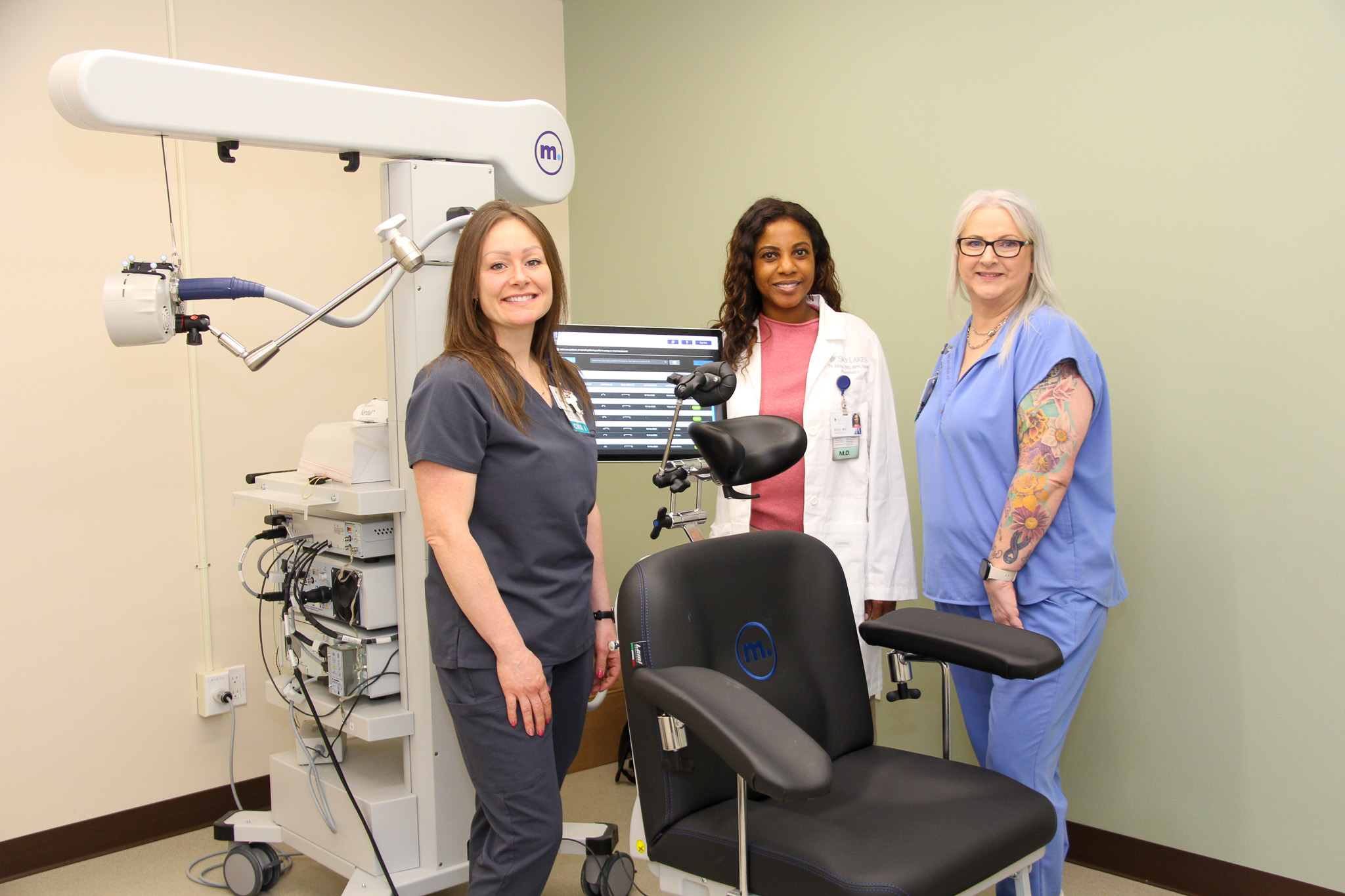 TMS group photo Three clinical employees standing around a Transcranial magnetic stimulation (TMS) machine