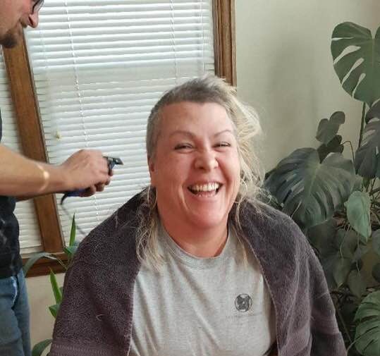 Middle aged woman smiling big while a man shaves her head for a cancer fundraiser for cancer treatment in Klamath Falls.